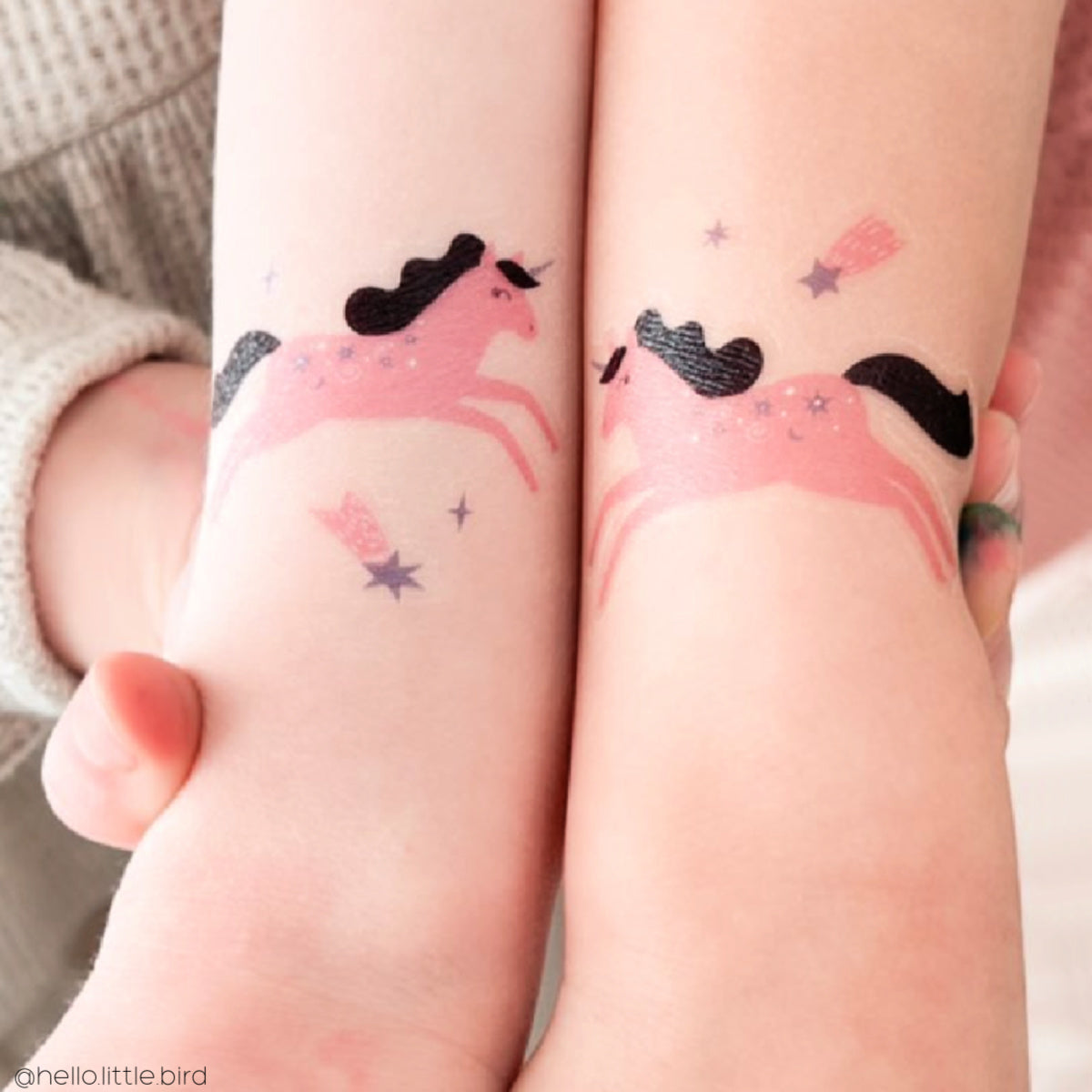 Children's arms with temporary tattoos of pink unicorns.