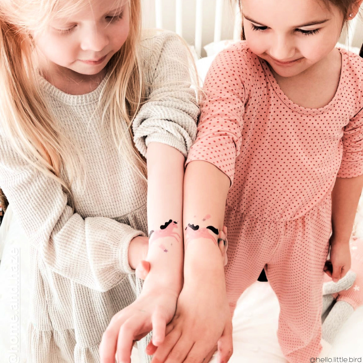 Two young girls showing off pink unicorns temporary tattoos on their wrists.