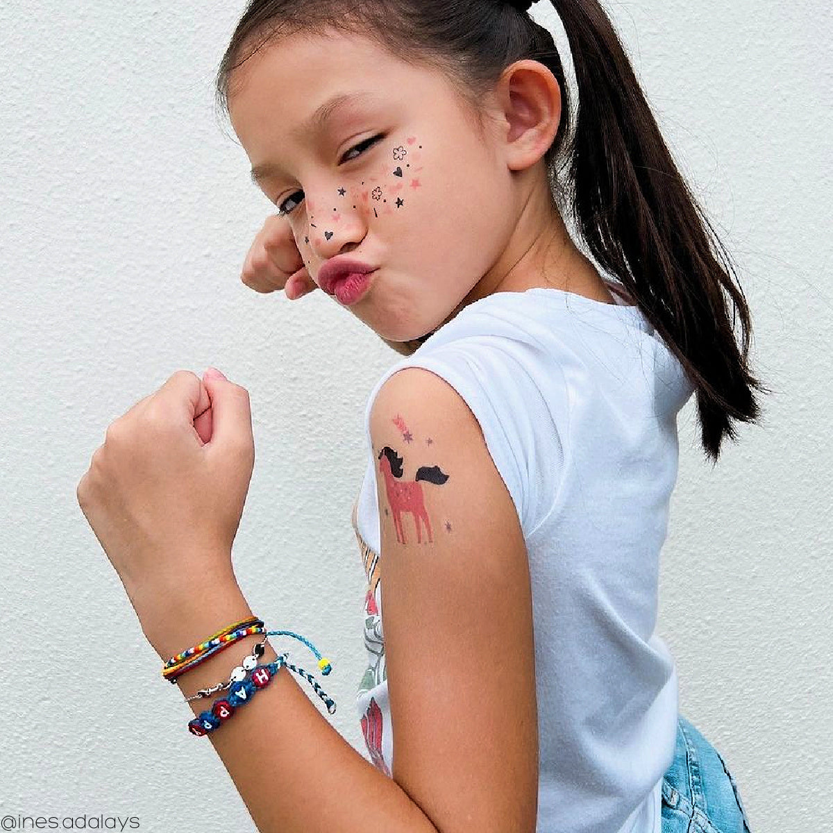 Young girl with a temporary tattoo of a pink unicorn on her arm and doodle freckles on her face.