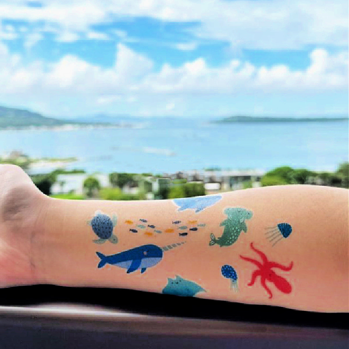 Colorful temporary tattoos of marine animals on a person's arm with a scenic background.