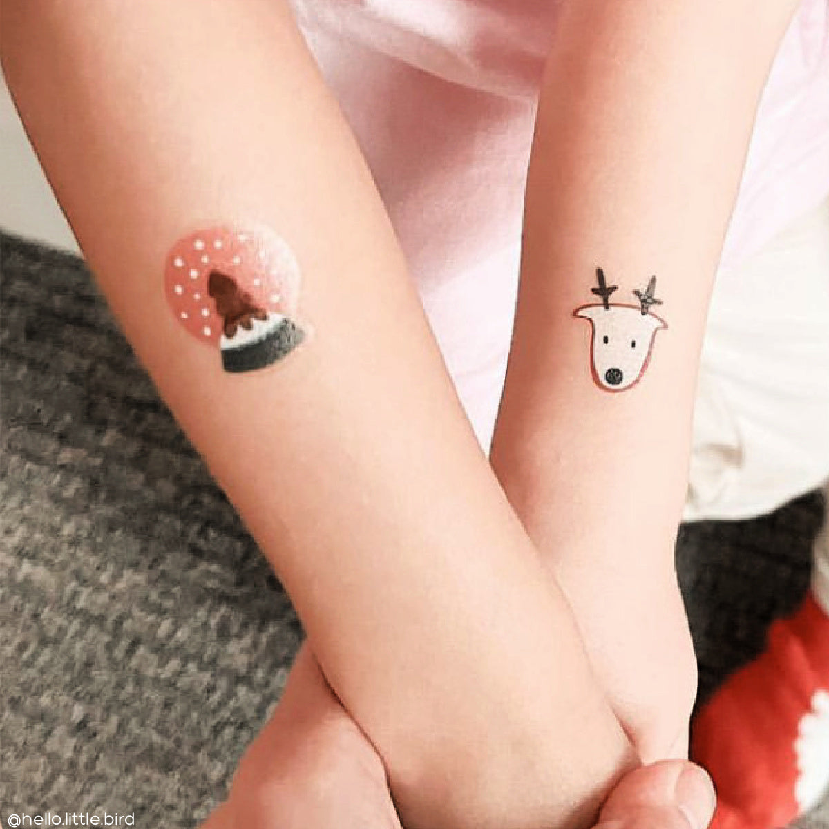 Two small temporary tattoos on a child's arm, one resembling a snow globe with a Christmas tree and snowflakes inside and the other a reindeer.