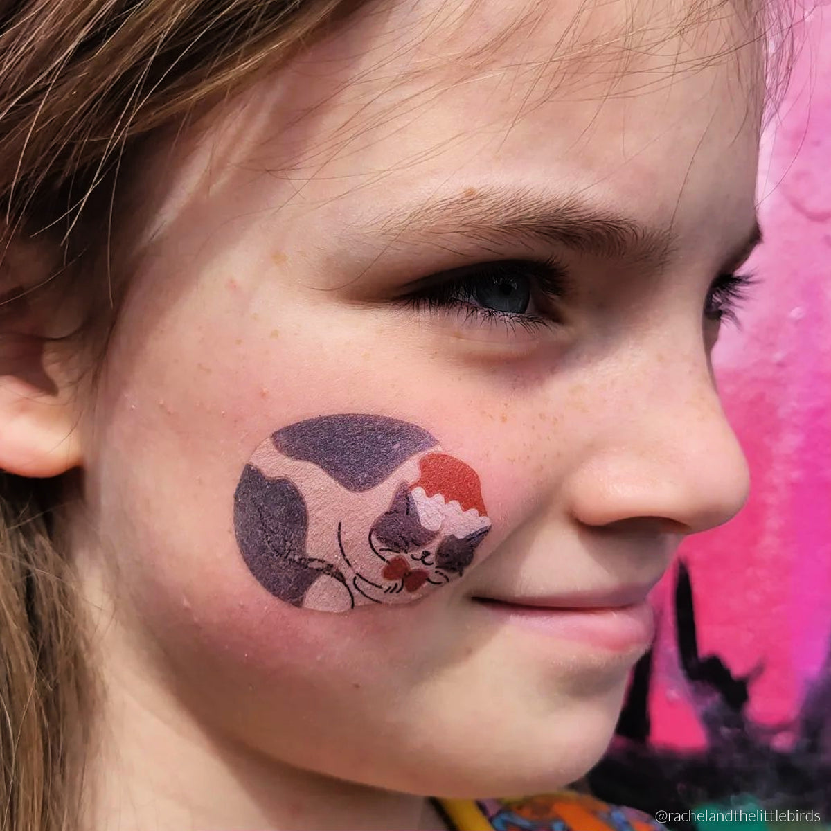 Young girl wearing temporary tattoo of a sleeping cat on her cheek.