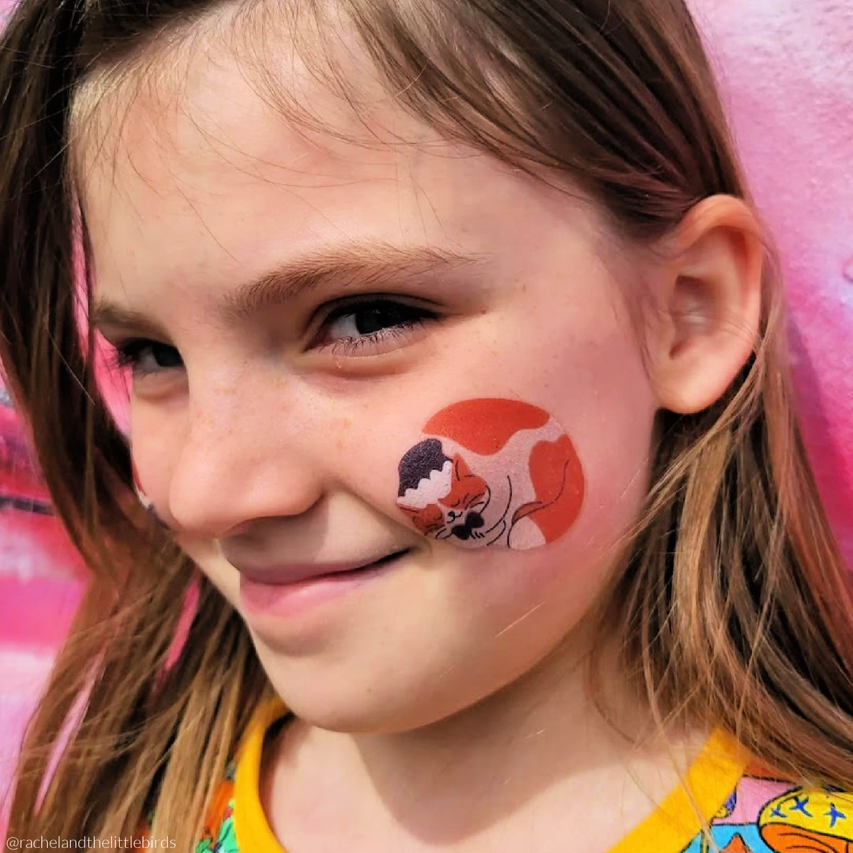 Young girl wearing temporary tattoo of a cat on her cheek.