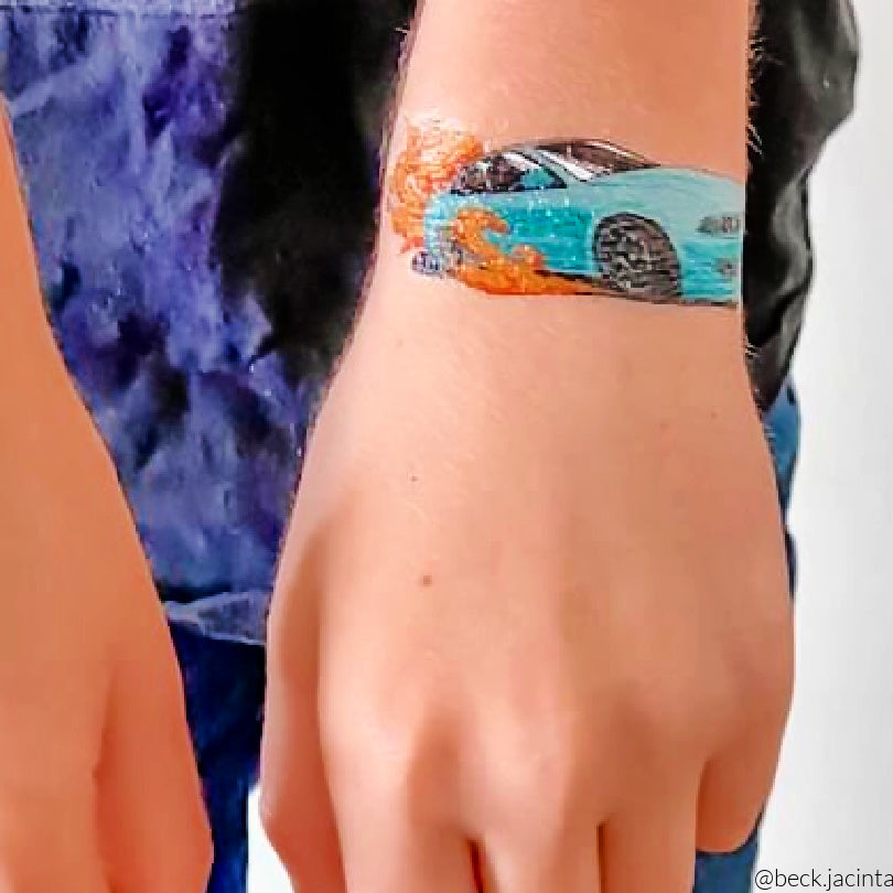 Colorful temporary tattoo of a blue car with red flames on a person's wrist with a blue shirt in the background.