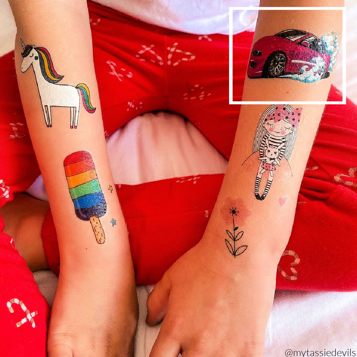 Child's arms covered with temporary tattoos of a unicorn, ice cream, pink doll, red car, pink flower.