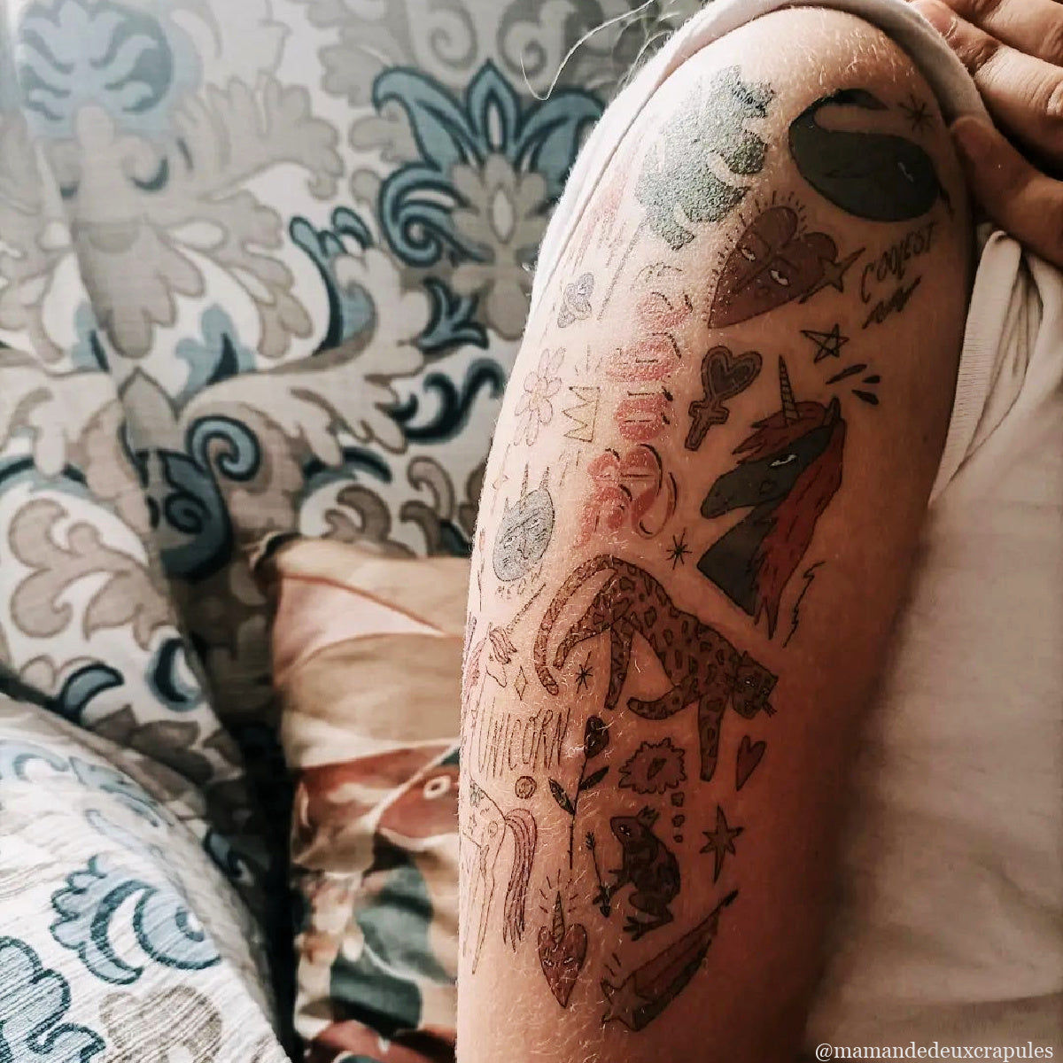 Person with temporary tattoos of cheetah, unicorn, hearts, text on the arm.