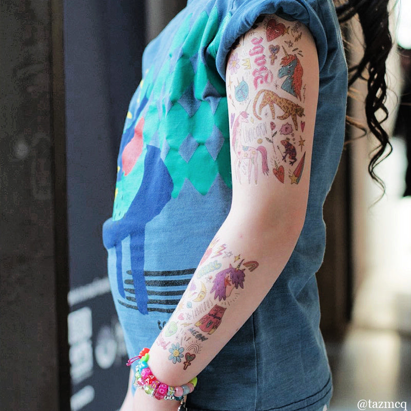 Young girl wearing a blue shirt with colorful temporary tattoos on her arm.